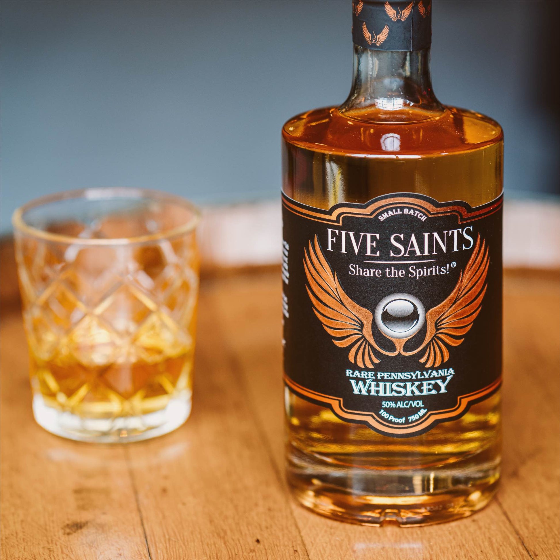 Five Saints Distilling Rare Pennsylvania Whiskey bottle beside a poured rocks glass on a wooden surface, showcasing the small batch 100 proof aged craft whiskey