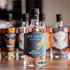 Five Saints Distilling White Whiskey bottle, a small batch spirit crafted from 75% corn and 25% rye mash, with other spirits bottles blurred in the background