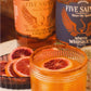 Spicy Confession cocktail in a rocks glass with blood orange garnish, served alongside Five Saints White Whiskey and Blood Orange Liqueur bottles