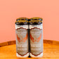 Four bottles of Five Saints Rum Mule canned cocktails on a wooden surface against a peach-colored background.