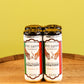 Four bottles of Five Saints Savory Tuscan Style Gin & Tonic canned cocktails on a wooden surface against a yellow-green background.
