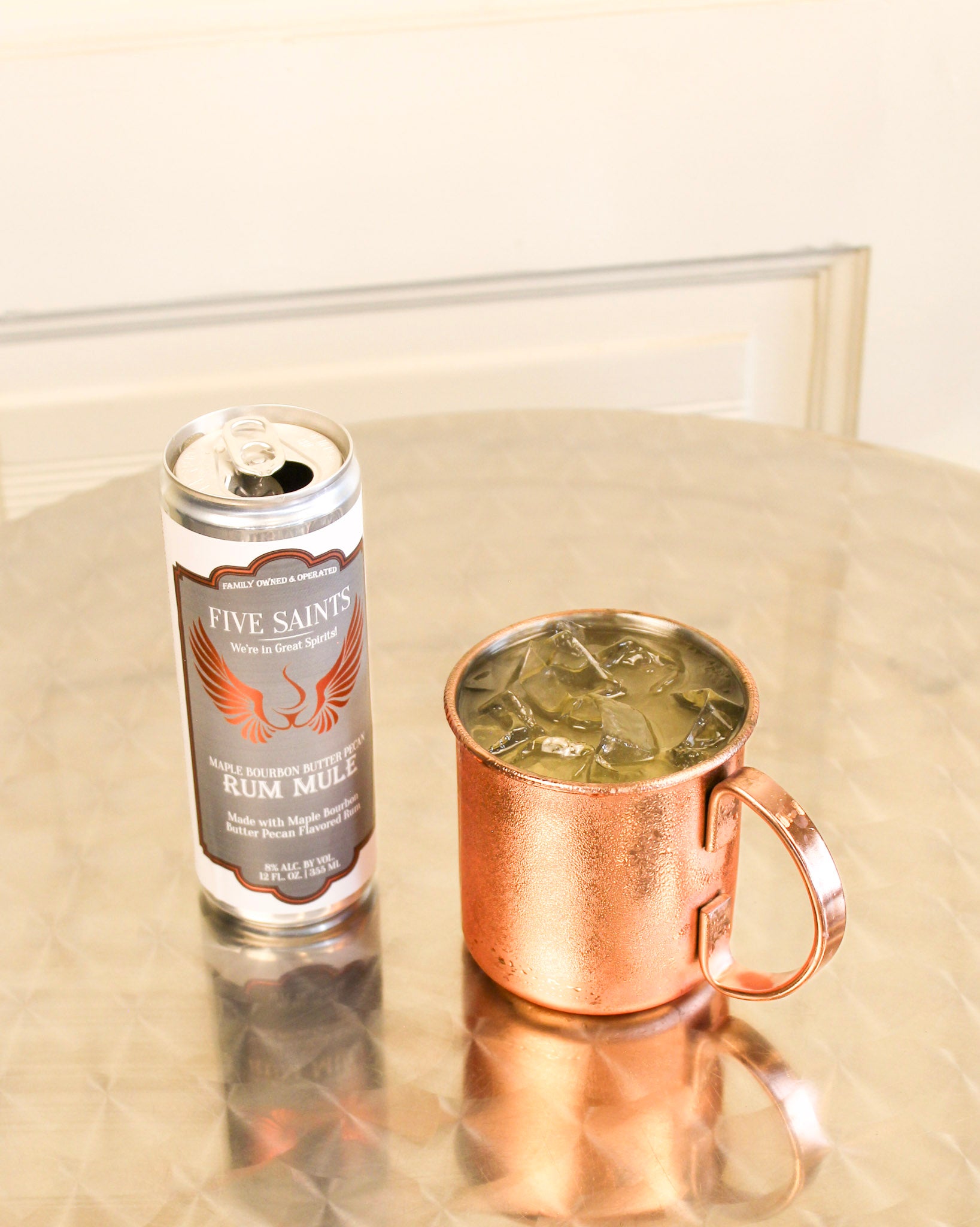 A can of Five Saints Rum Mule and a copper mule mug, set on a reflective metallic table