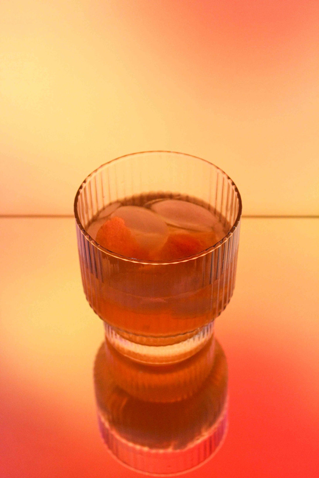 Clear glass with a drink and ice cubes on a gradient orange to red background